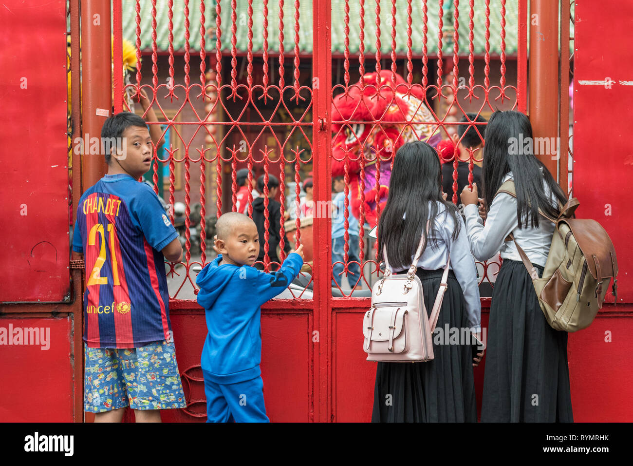 Children stand along a metal gate with forged bars painted red including a boy who has facial features of a person with Down syndrome - Phnom Penh. Stock Photo