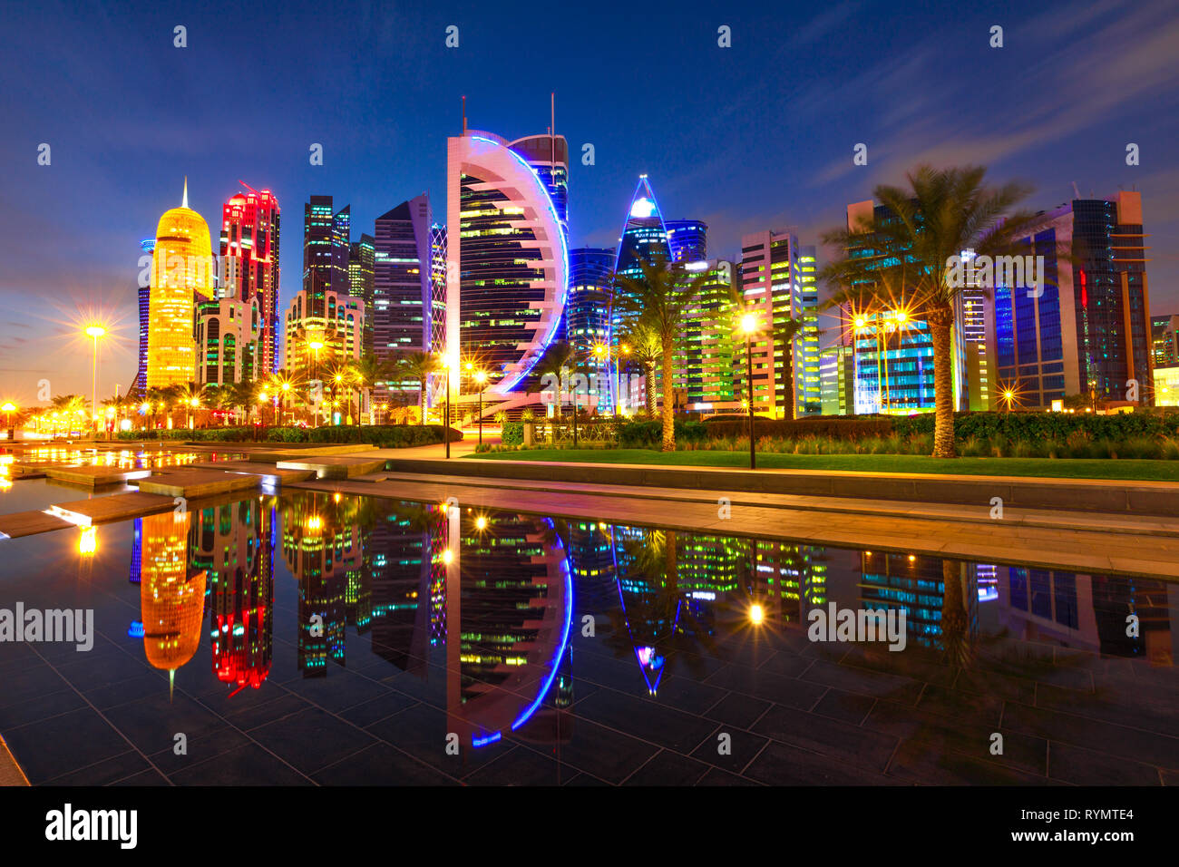Doha West Bay high rises illuminated by night reflecting in the water of park in Downtown. Modern skyscrapers of Doha skyline, Qatar, Middle East Stock Photo