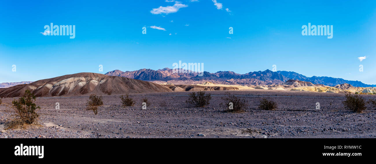 Rocky desert landscape with space vegetation and barren hills under a bright blue sky. Stock Photo