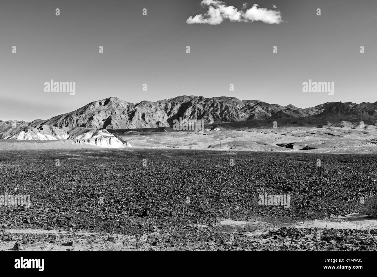 Rocky desert fields with barren mountains beyond, white fluffy clouds. Black and white. Stock Photo