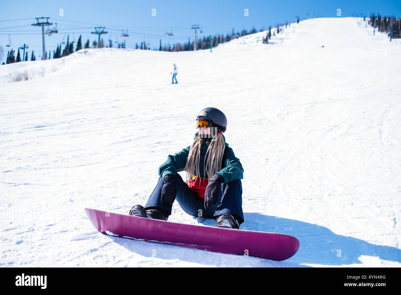 Young woman snowboarder sitting on a snowy slope. Stock Photo