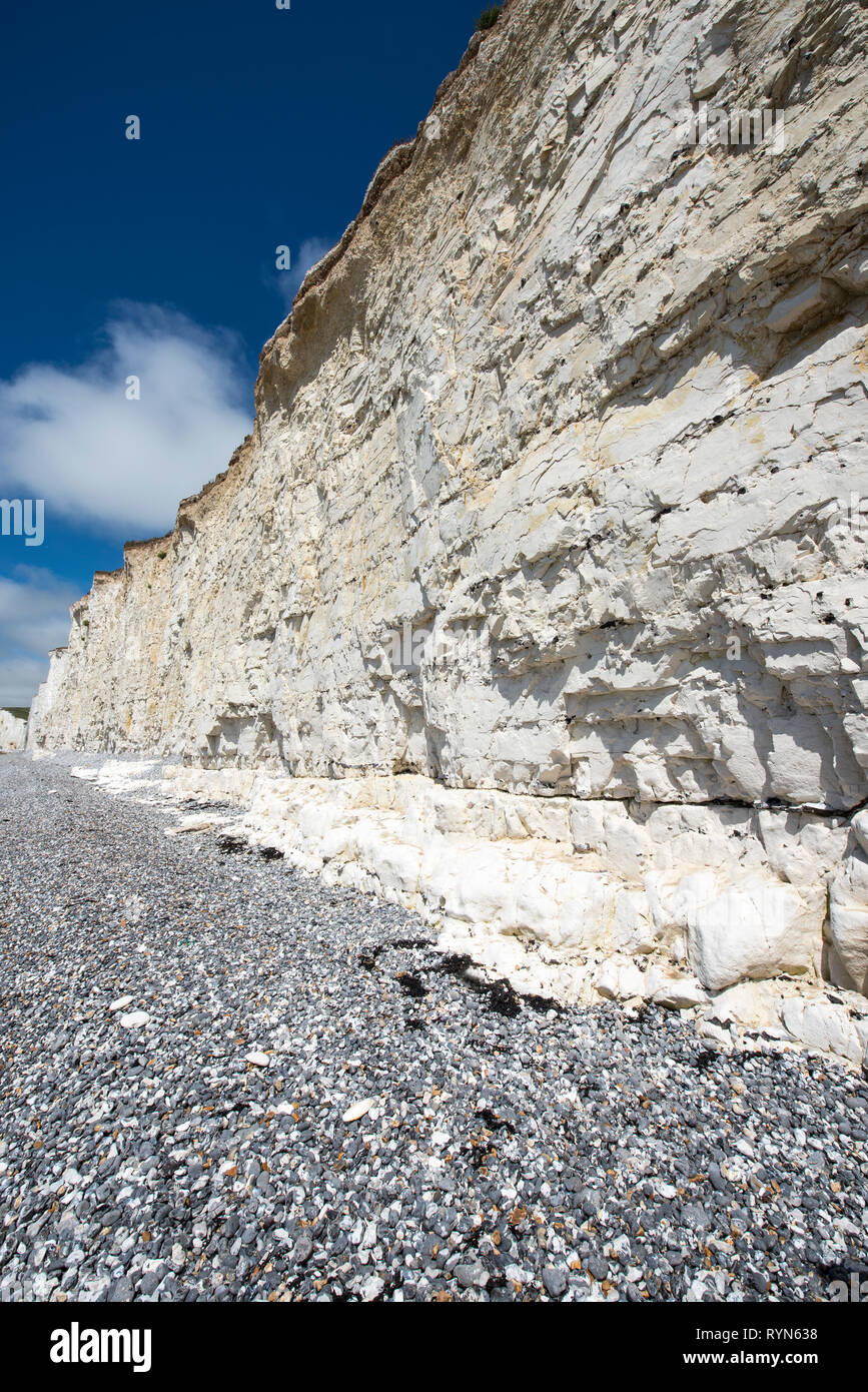 White chalk rock wall at Birling Gap, Sussex, with clear sediment layers and pebble beach beneath, sunny and blue sky, wide angle Stock Photo