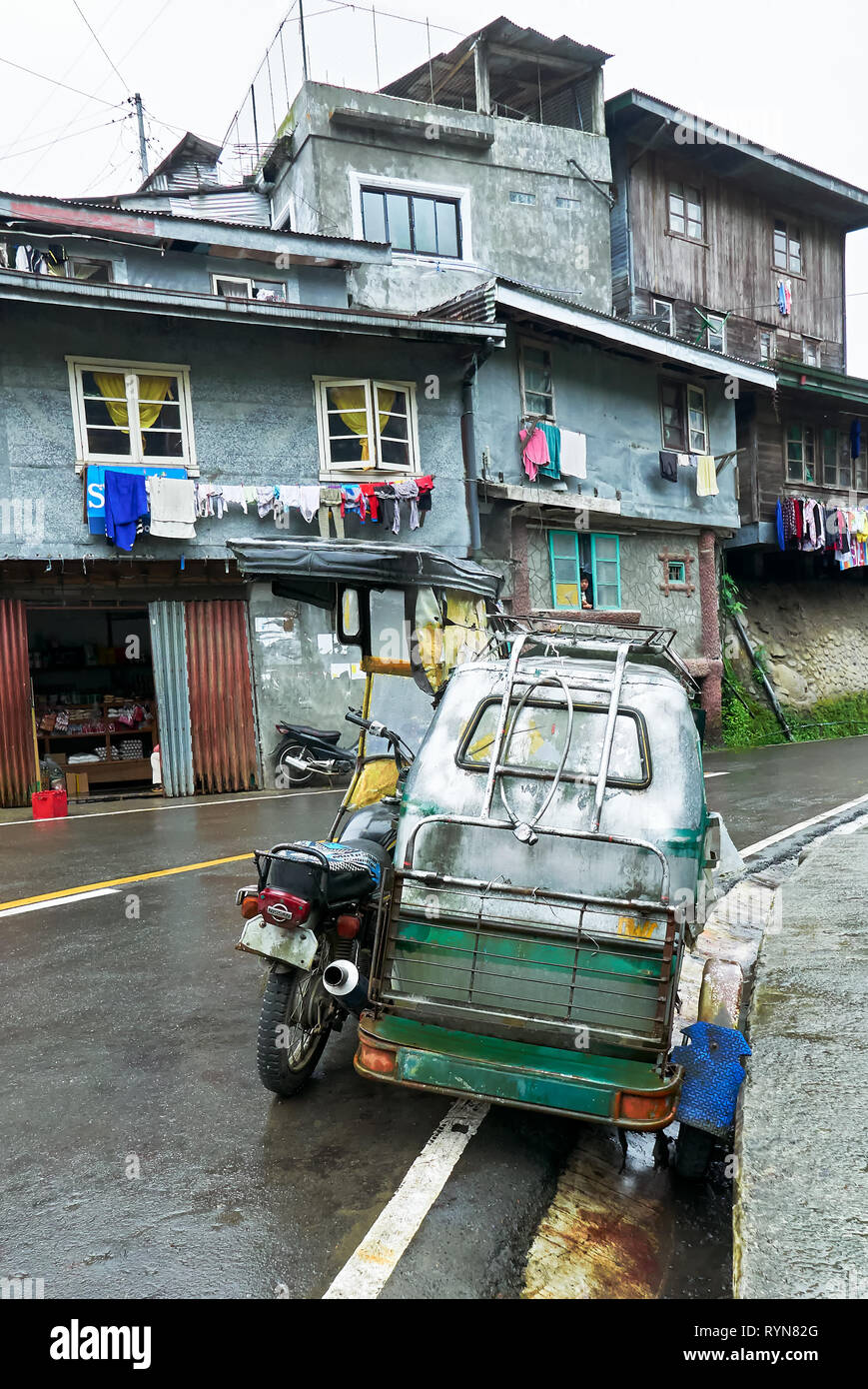 A Motorcycle with sidecar parking along a curved road in Banaue Town, Ifugao Province, Philippines, with typical simple buildings in the background. Stock Photo