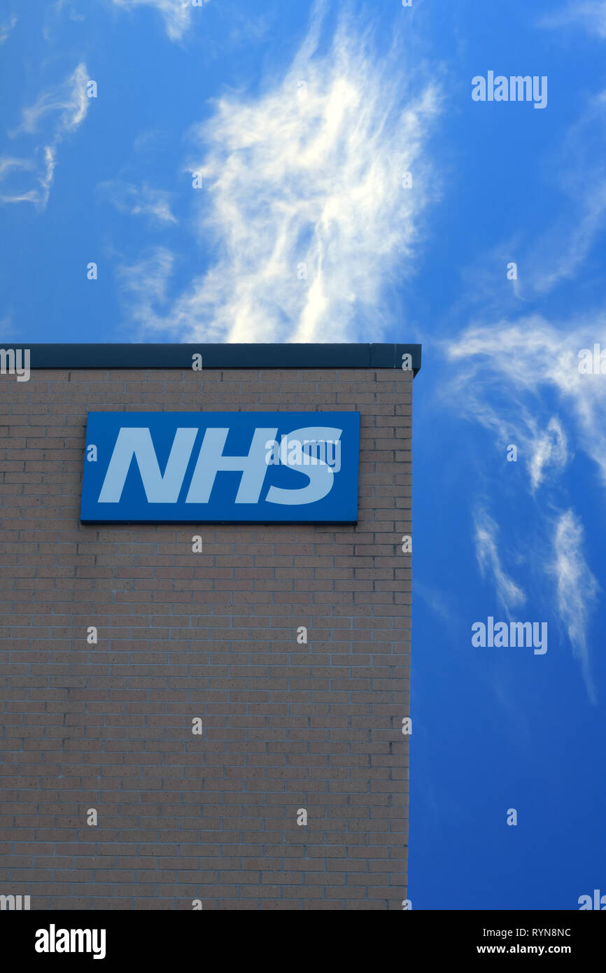 NHS sign on the outside wall of a  UK health centre building against a blue sky. Stock Photo