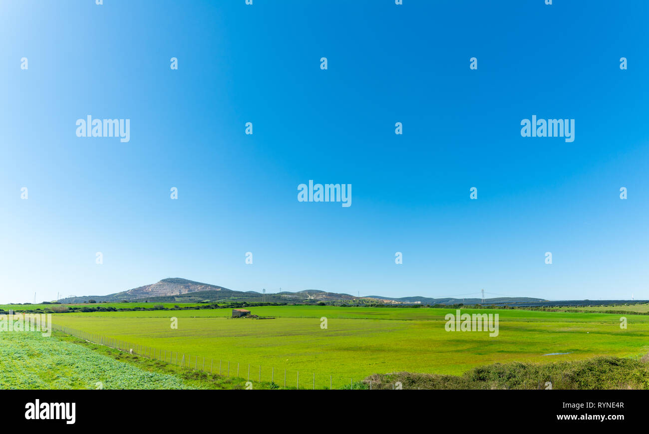 country landscape with a big meadow and small house in a sunny day of spring Stock Photo