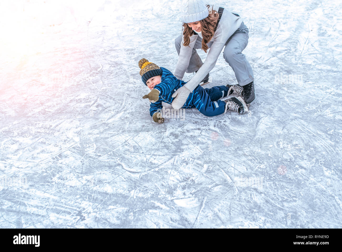 The baby fell on the ice. A young mother skates in the park in winter, with her son a young child 3-5 years old. Weekend rest at a public skating rink Stock Photo