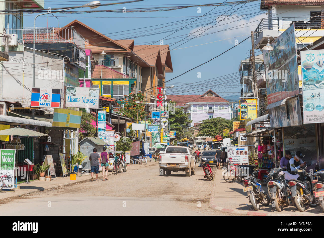 One of the central streets of Vang Vieng City with its chaotic architecture and the abundance of sign boards of different sorts of tourism businesses. Stock Photo