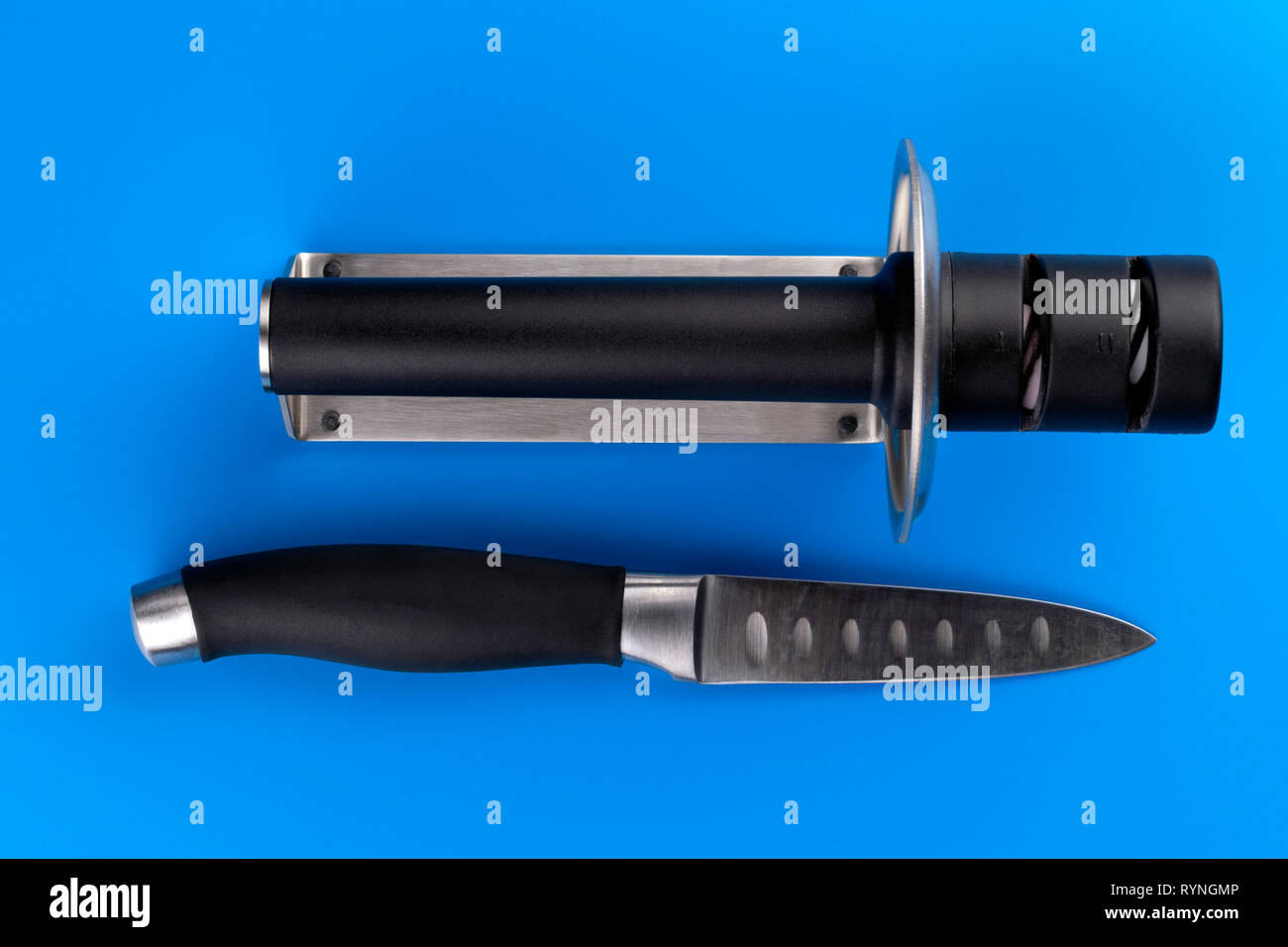 Knife and knife sharpener on a blue surface. Kitchen tools isolated on white background. Stock Photo