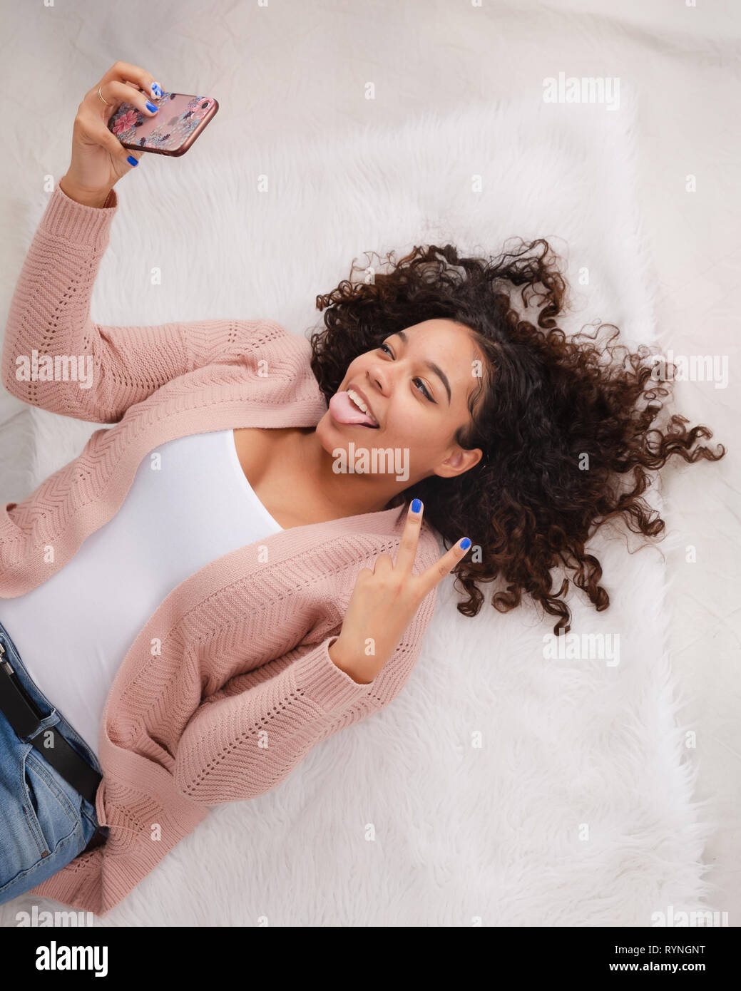 Attractive biracial high school senior laying down on floor smiling and posing for selfie to go on social media Stock Photo
