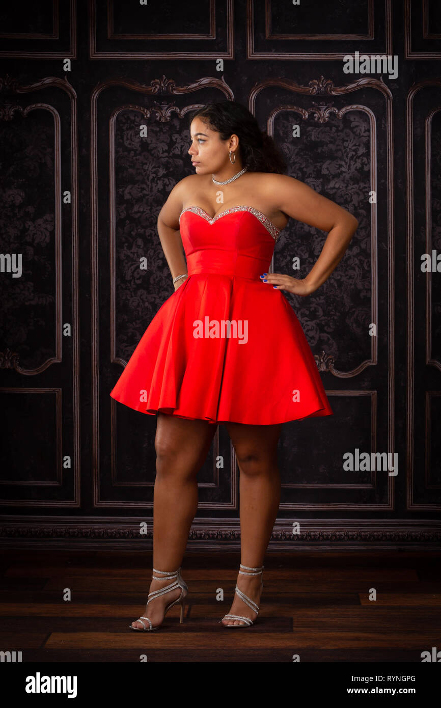 One beautiful,  biracial high school senior girl wearing red party dress waiting and looking away. Stock Photo