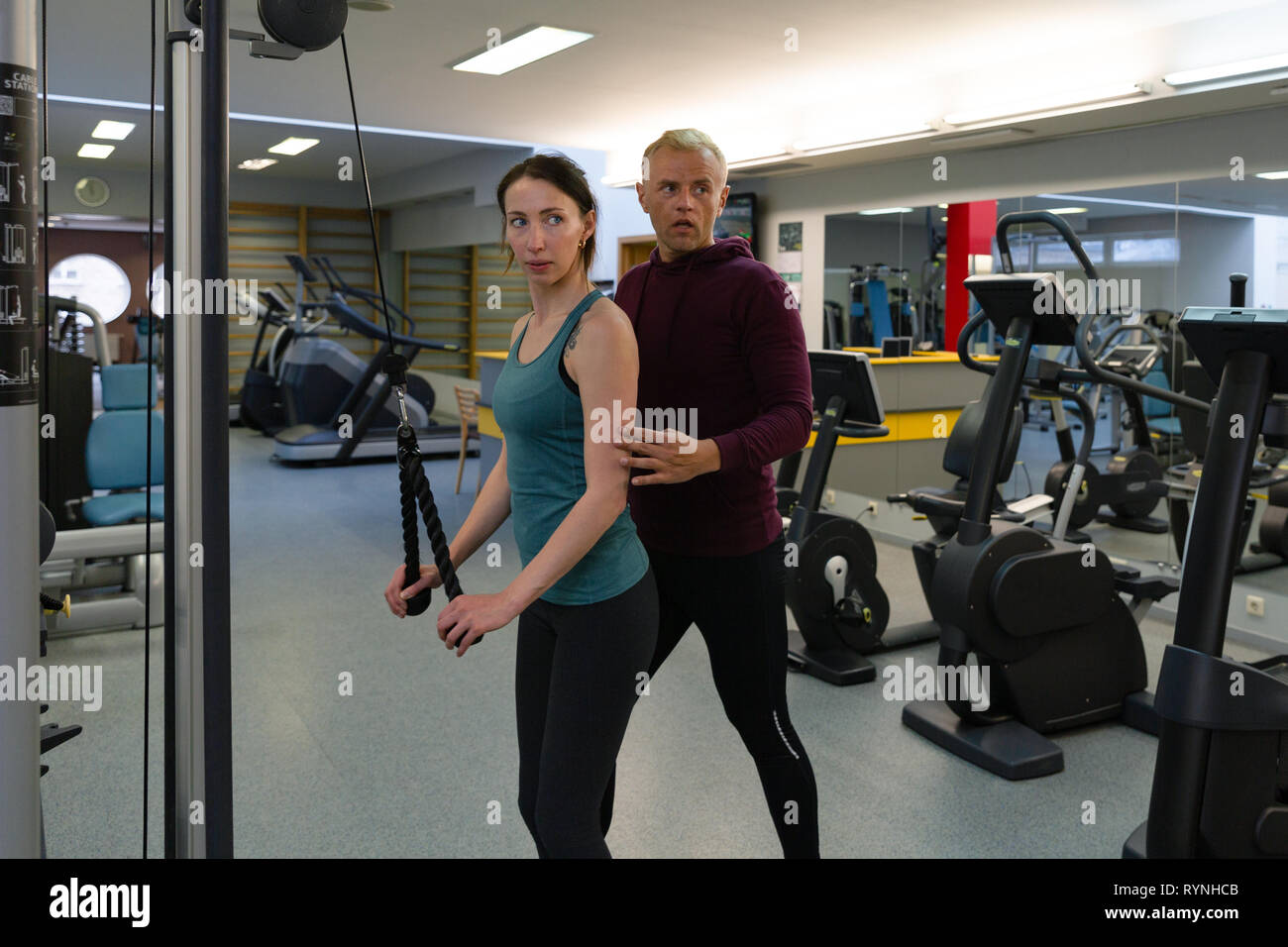 Young beautiful woman doing exercises with personal trainer. Young adult personal fitness trainer supporting his client at gym Stock Photo