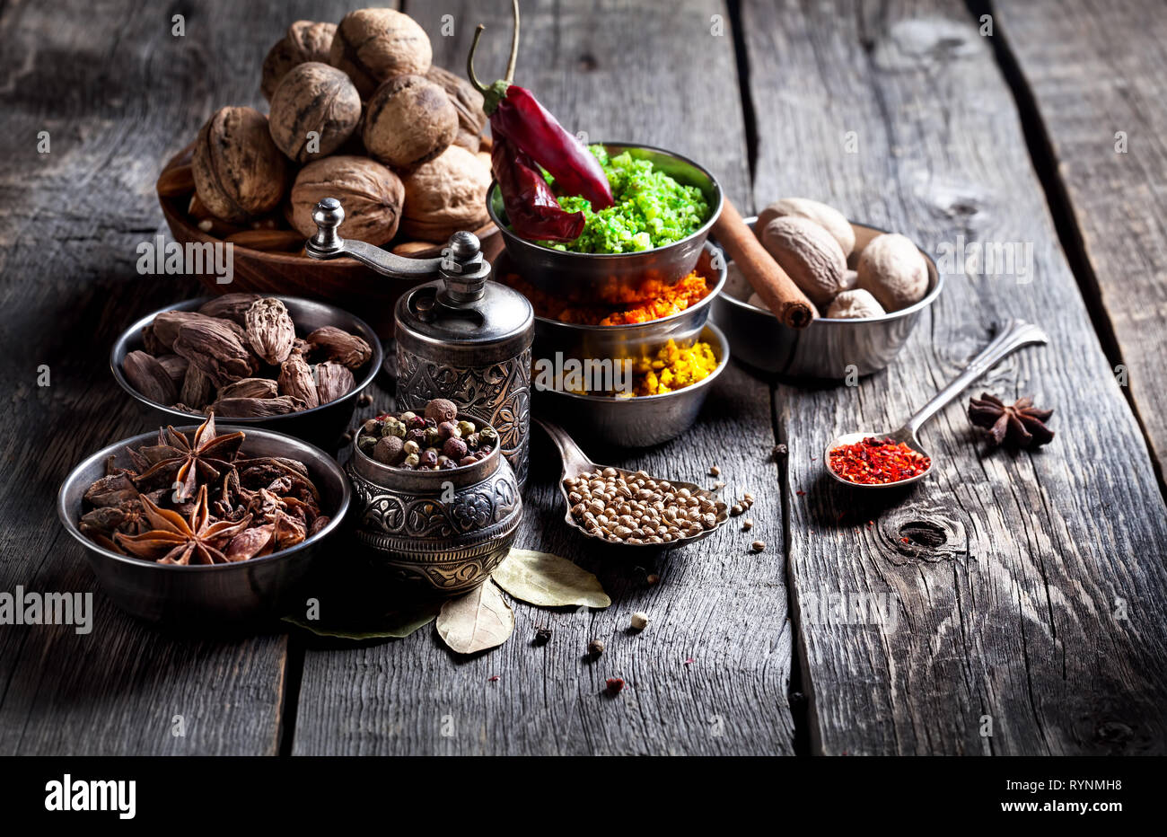 Spices, pepper grinder, spoon with seeds at grey wooden background