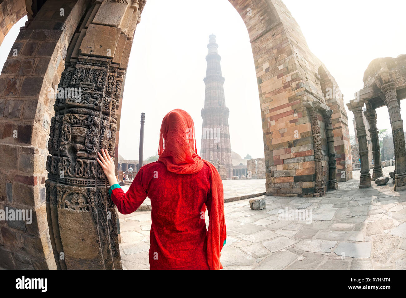 Woman in red costume looking at Qutub Minar tower in Delhi, India Stock Photo