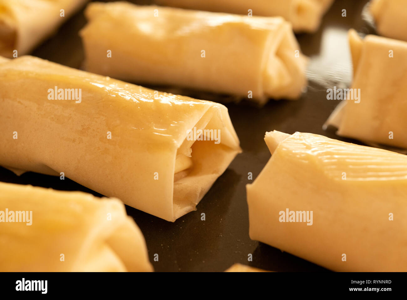 Rows of raw puff pastry cheese bites turnovers on black baking tray. Uncooked puff pastries close up of puff pastry sheets cheese bites Stock Photo