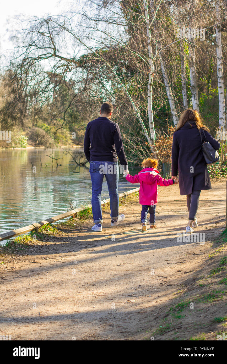 family on a walk in the park. father and mom holding their daughter arms. Family walk down the path in the park Stock Photo
