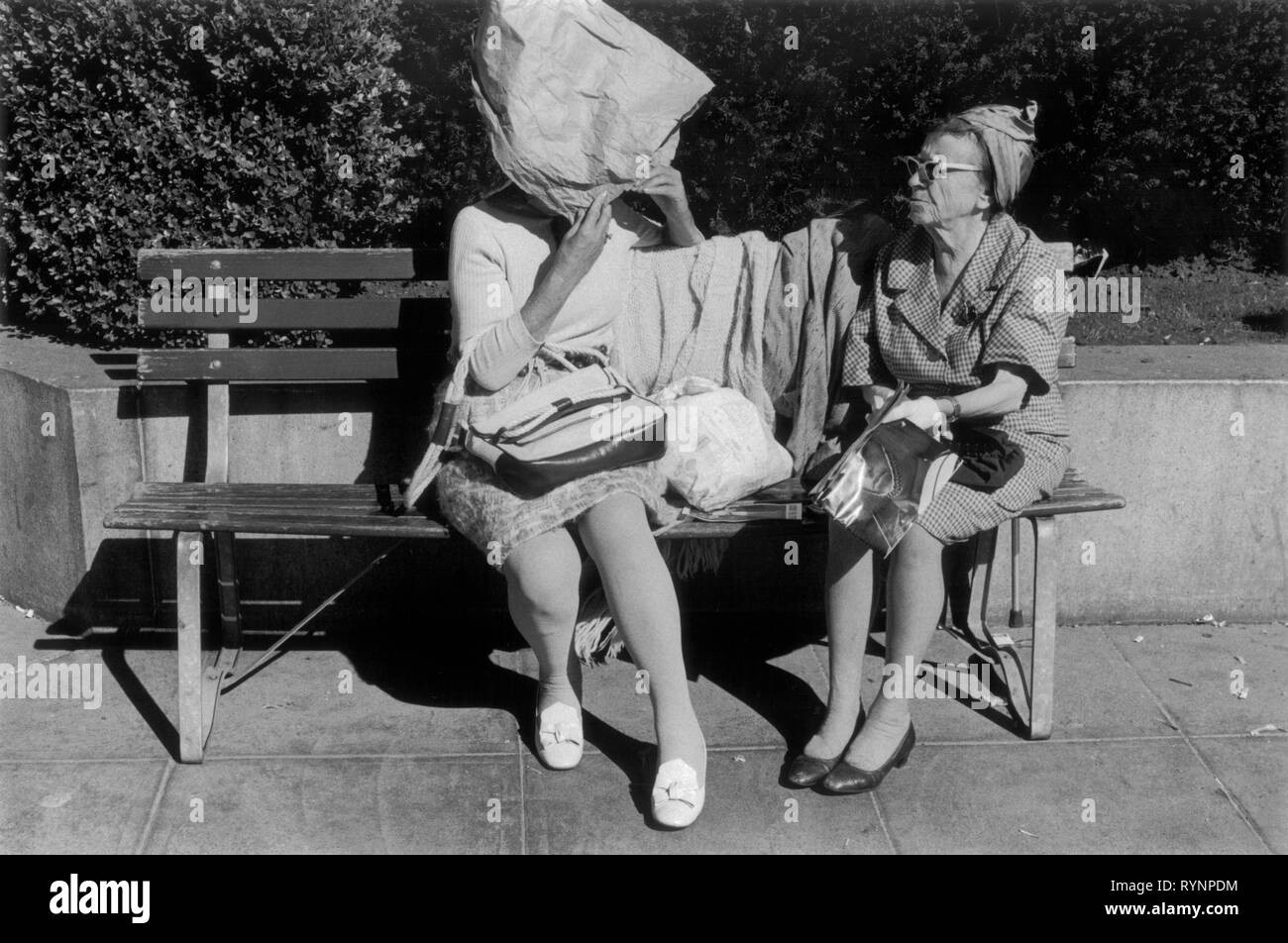 Two older women chatting in a downtown park, one has made a bonnet  from a brown paper bag to shield herself from the sun. San Francisco, California. 1971 1970s people, USA HOMER SYKES Stock Photo