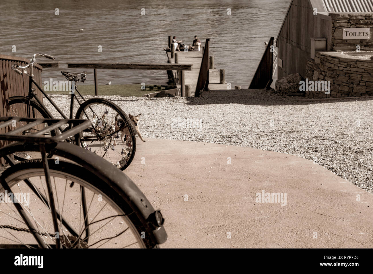 CROMWELL, NEW ZEALAND - OCTOBER 21 2019; Old bicyle wheels in street in small town with group four youth in distance on jetty on Lake Dunstan aged ima Stock Photo