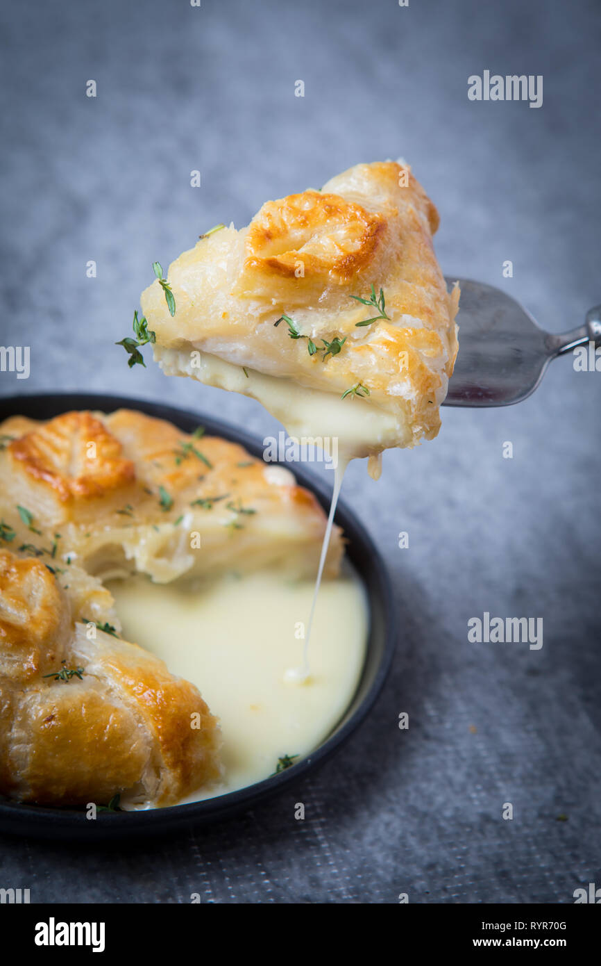 Slice of fried camembert cheese in puff pastry crust and oozing cheesy center. Camembert en croute is a traditional cheese French starter shot on a gr Stock Photo