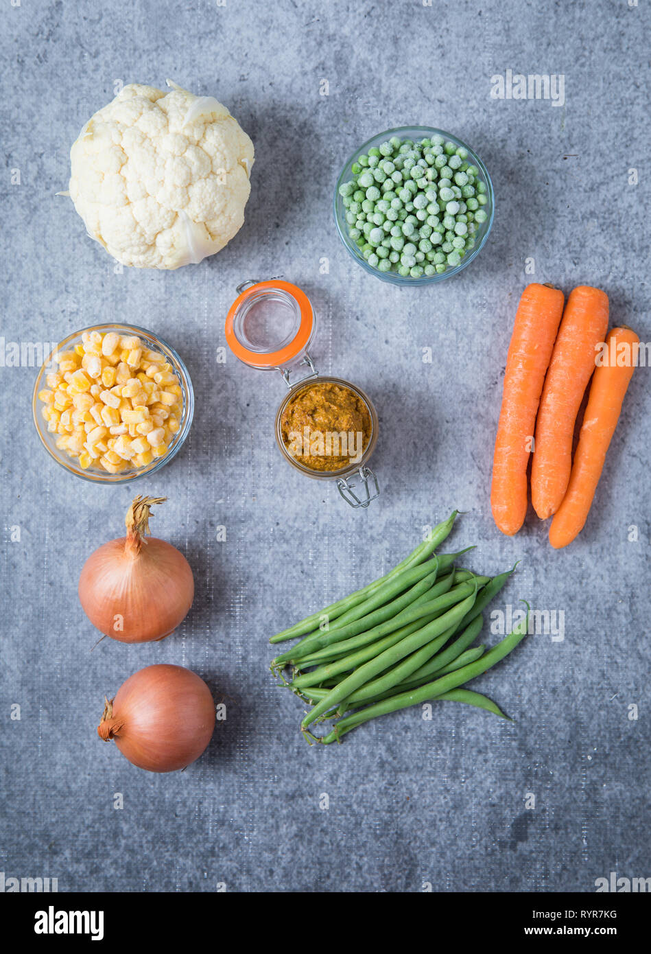 Ingredients for onion curry paste on light grey background. Picture of two onions, cauliflower, peas, corn, green beans and carrots on grey background Stock Photo