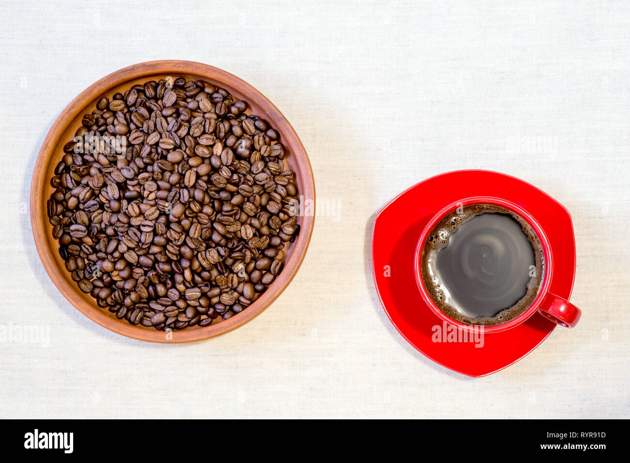 Red mug of freshly brewed coffee with roasted beans in a ceramic clay pan on linen canvas. Top view, flat lay. Stock Photo