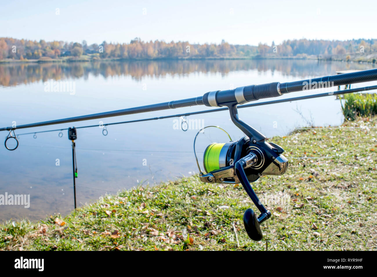 Close-up of shiny metal reels of pair of fishing rods on stands fixed into  ground of grass covered lake edge at Surrey, United Kingdom Stock Photo -  Alamy
