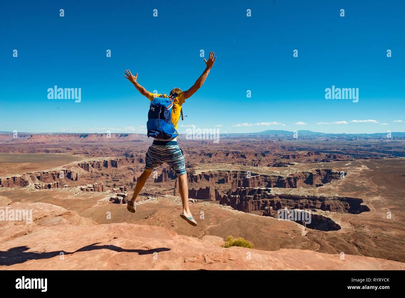 Young man jumping with outstretched arms, view from Grand Viewpoint, rugged gorges of the Green River, canyon landscape Stock Photo