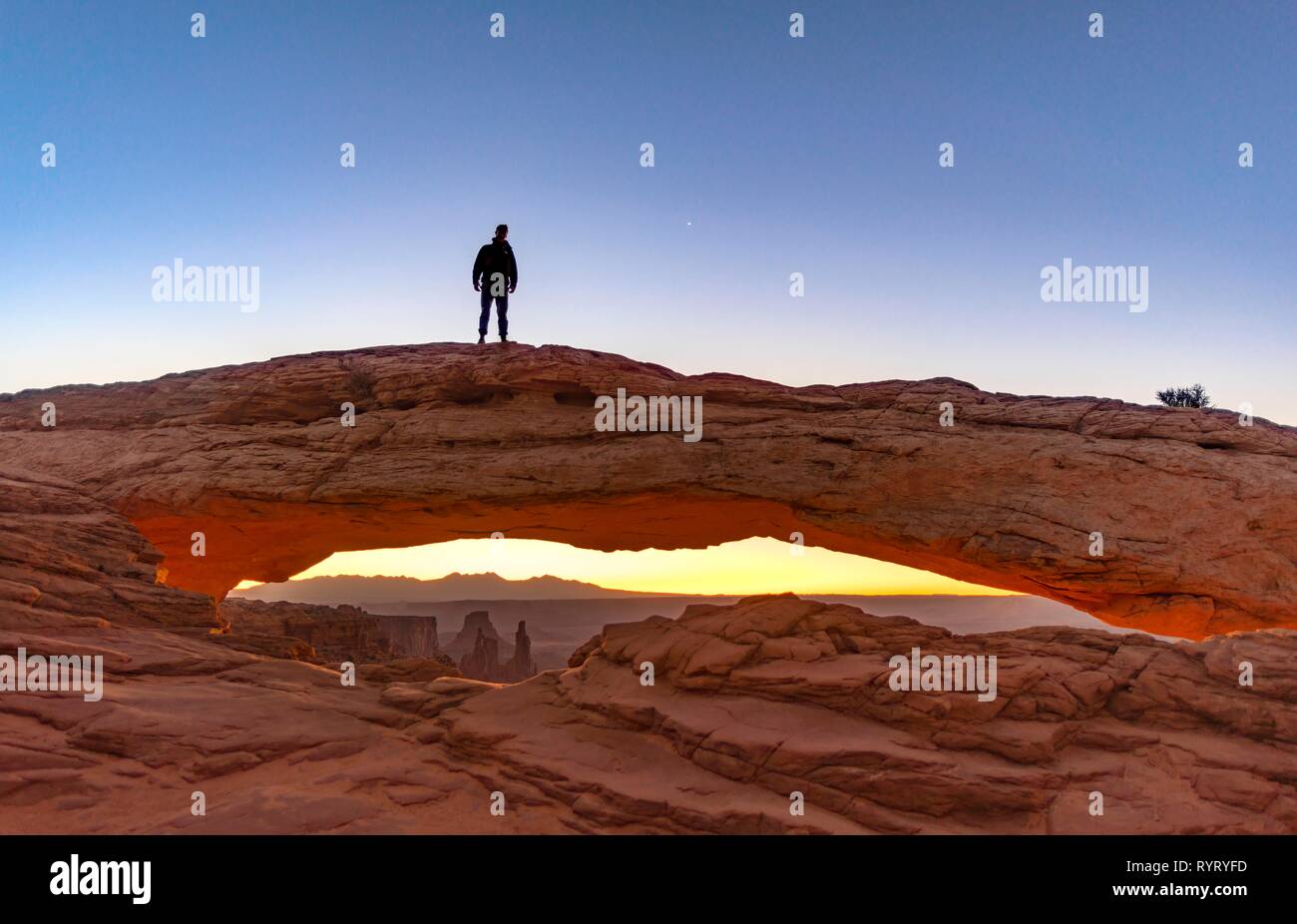 Young man standing on rock arch, Mesa Arch, sunrise, Grand View Point Road, Island in the Sky, Canyonlands National Park, Moab Stock Photo
