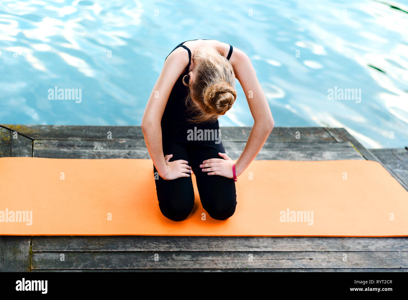 little girl doing yoga on the river bank. the child is engaged in pilates on an orange mat near the lake. healthy lifestyle Stock Photo