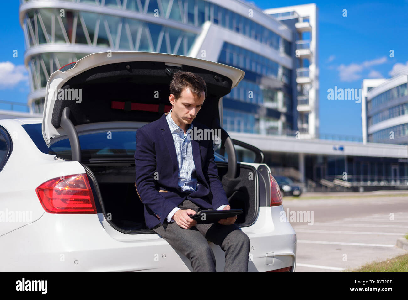 successful young businessman freelancer working outside in the city. man sit on car boot with tablet laptop Stock Photo