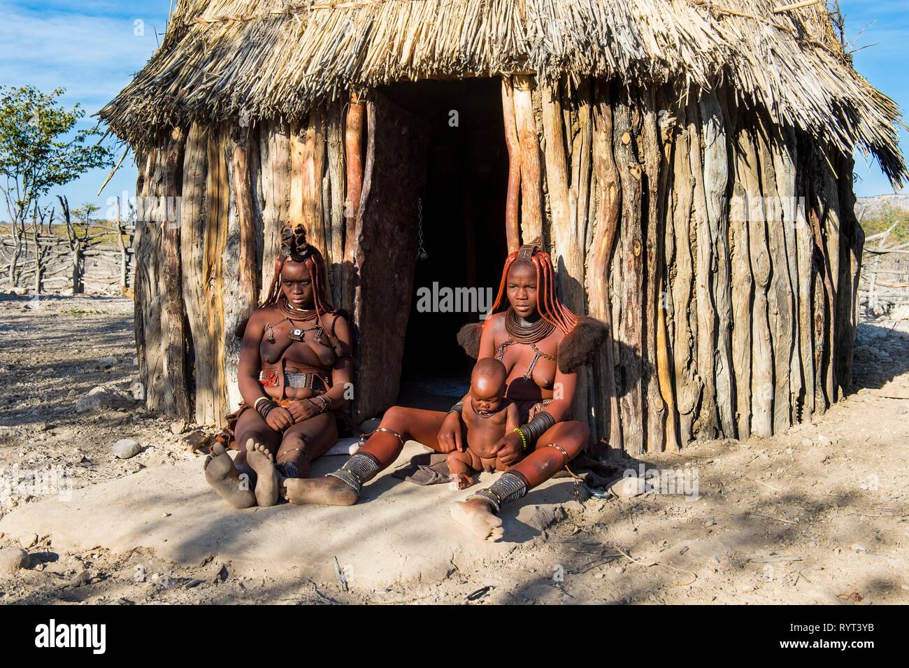 Himba women in front of their hut, Kaokoland, Namibia Stock Photo