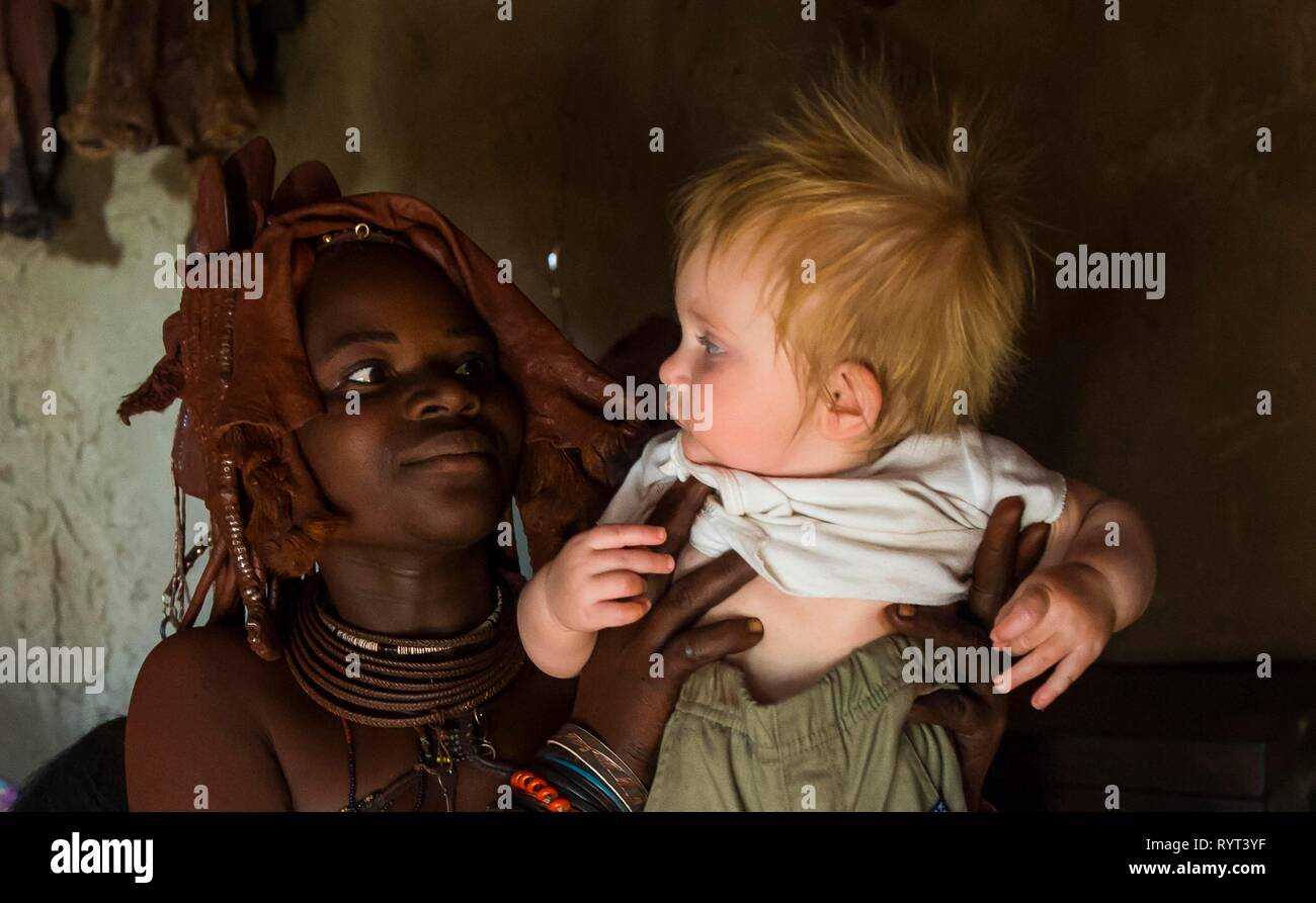 Himba woman holding a white tourist baby, Kaokoland, Namibia Stock Photo