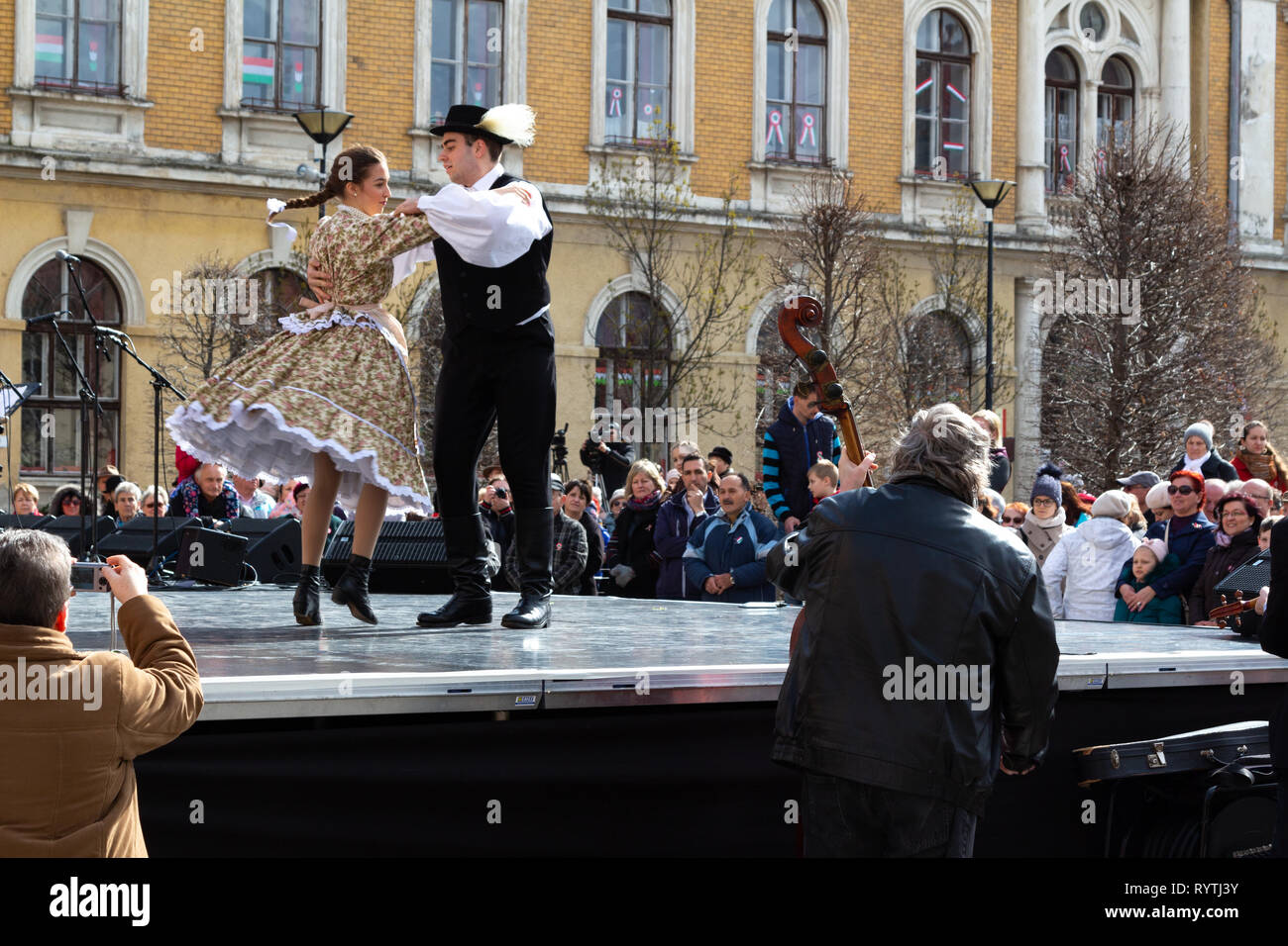 Sopron, Hungary. 15th Mar, 2019. A couple of folk dancers performs traditional Hungarian dances on stage at Petőfi Square, Sopron, Hungary. Feather grass (stipa) is sticked in the lad's hat as it was used in the old times. Credit: Wahavi/Alamy Live News Stock Photo