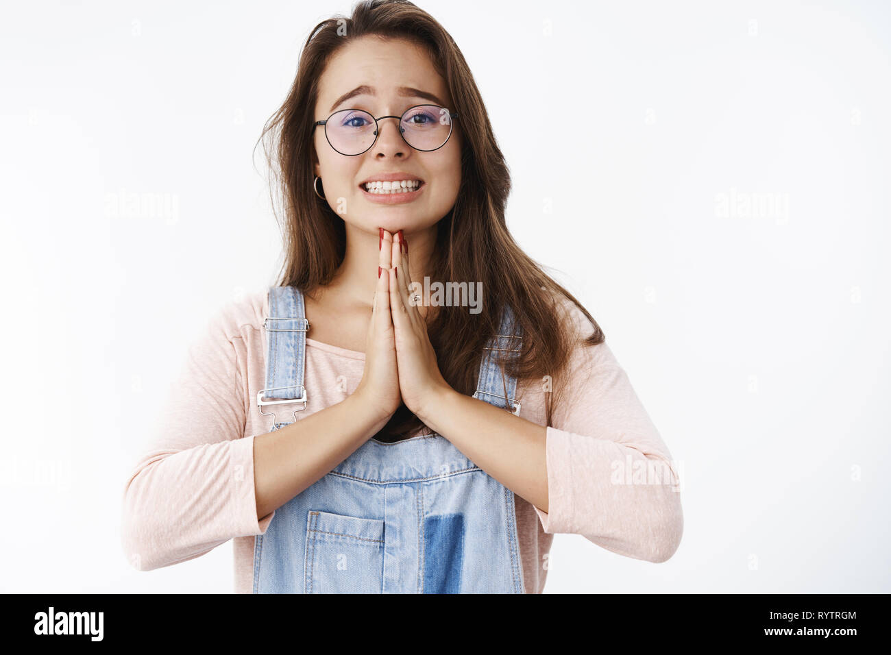 Close-up shot of sad and hopeful attractive woman in glasses standing in begging pose holding hands in pray expressing suppolication as wanting Stock Photo