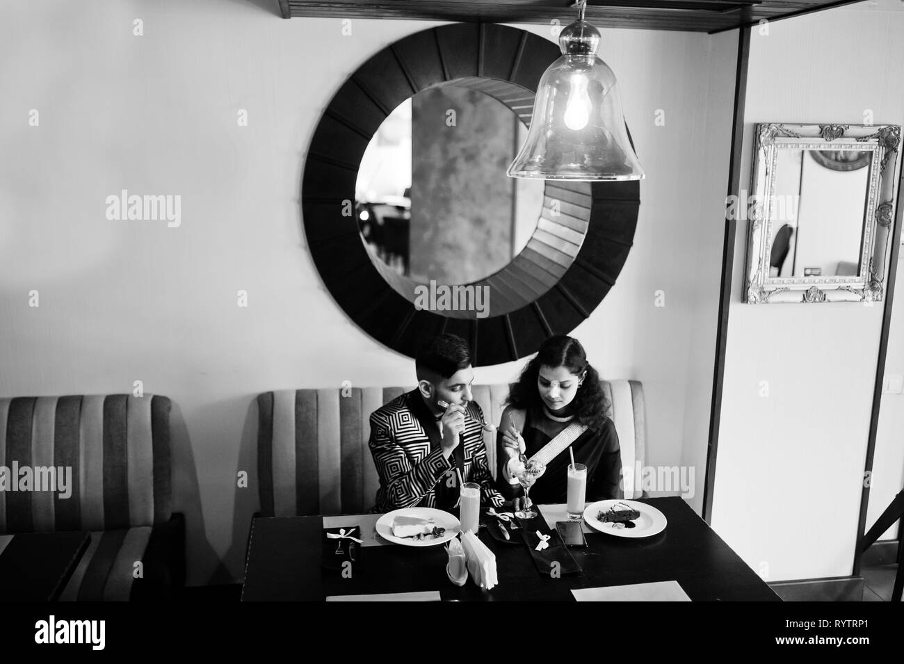 Lovely indian couple in love, wear at saree and elegant suit, sitting on restaurant and  eating ice cream together. Stock Photo