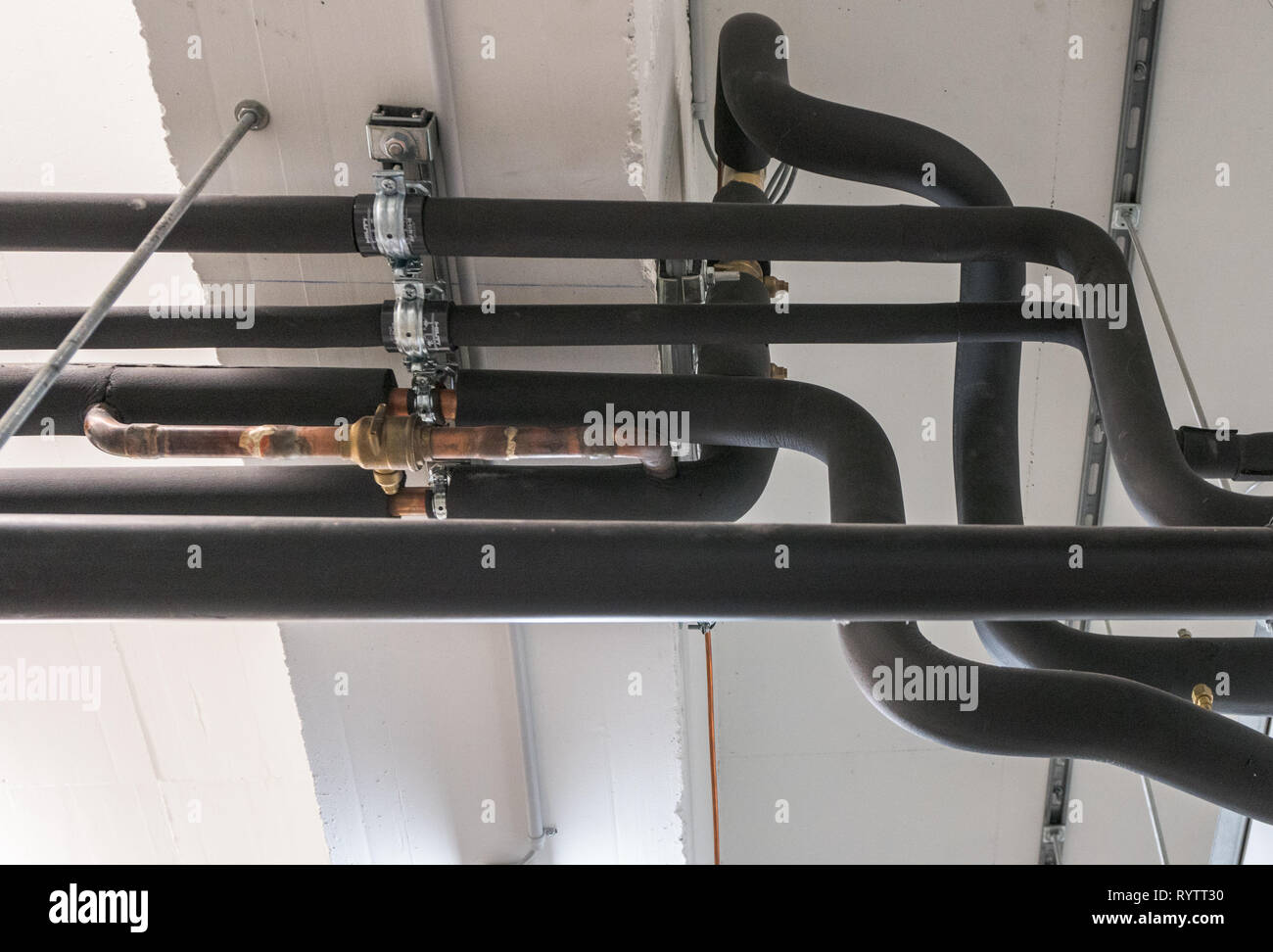 metal and plastic pipe system on the cellar ceiling of an apartment building with water and heating pipes Stock Photo