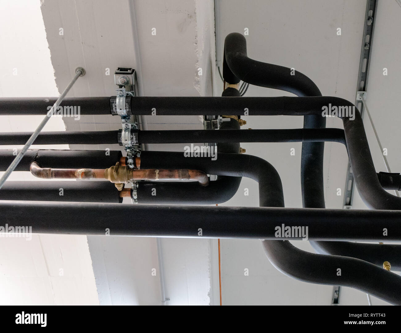 metal and plastic pipe system on the cellar ceiling of an apartment building with water and heating pipes Stock Photo