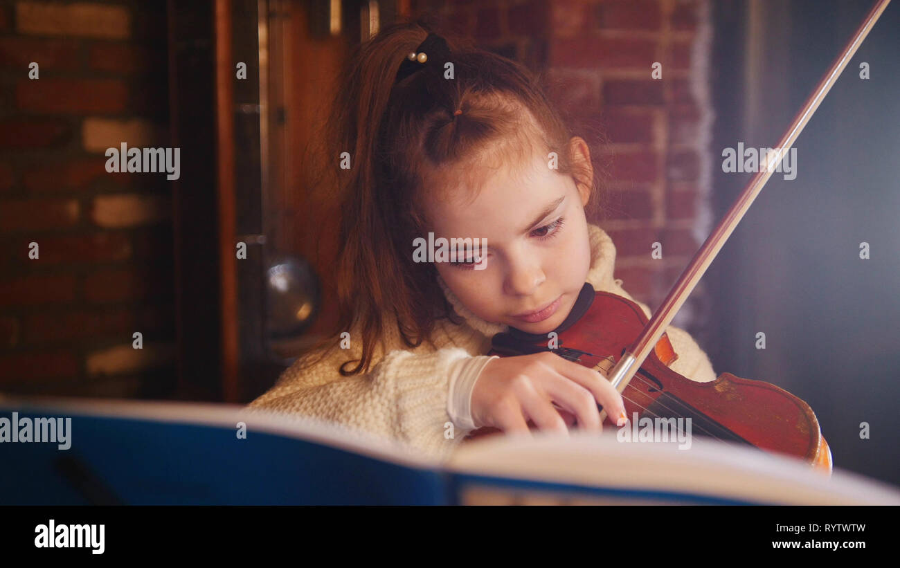 A little girl in white sweater playing violin by notes Stock Photo - Alamy