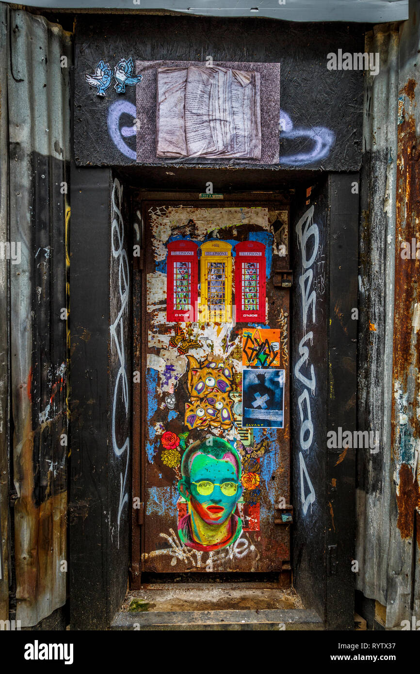 Padlocked steel doorway within an alcove. Posters and graffiti with corrugated sheet metal. Stock Photo