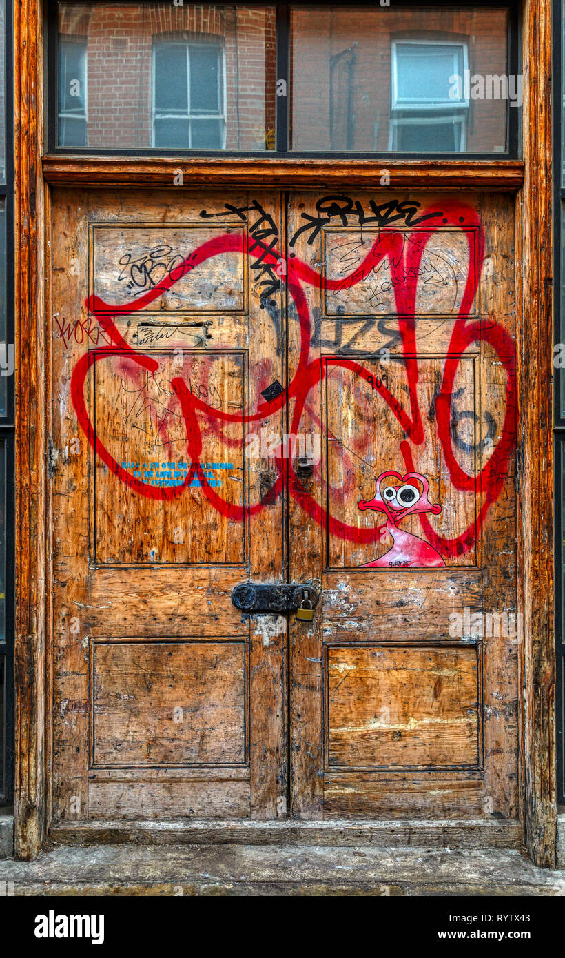 Wooden double door into a property within London's East End. Padlocked and tagged with graffiti. Stock Photo