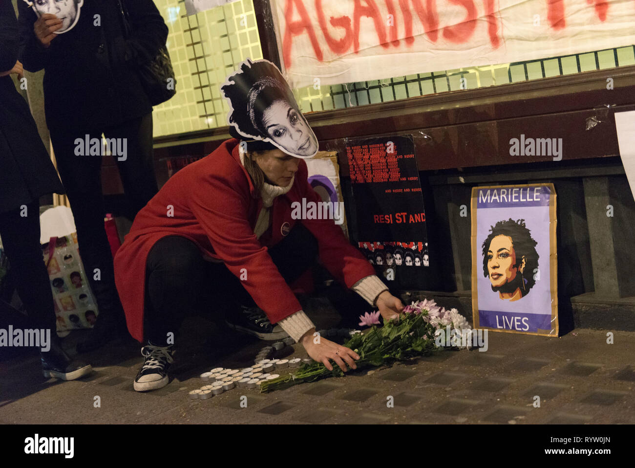A woman seen putting flowers next to a poster with Marielle Franco image. Protesters gathered outside the Brazilian embassy in London to honor the life and legacy of Brazilian activist Marielle Franco who was an outspoken critic of police brutality and extrajudicial killings against favela residents. Franco was assassinated for her political activities along with her driver Anderson Gomes on March 14, 2018 in Rio de Janeiro, Brazil. During the vigil speakers addressed the assistants and claimed justice and demanded the end of the impunity in Franco's crime. Stock Photo