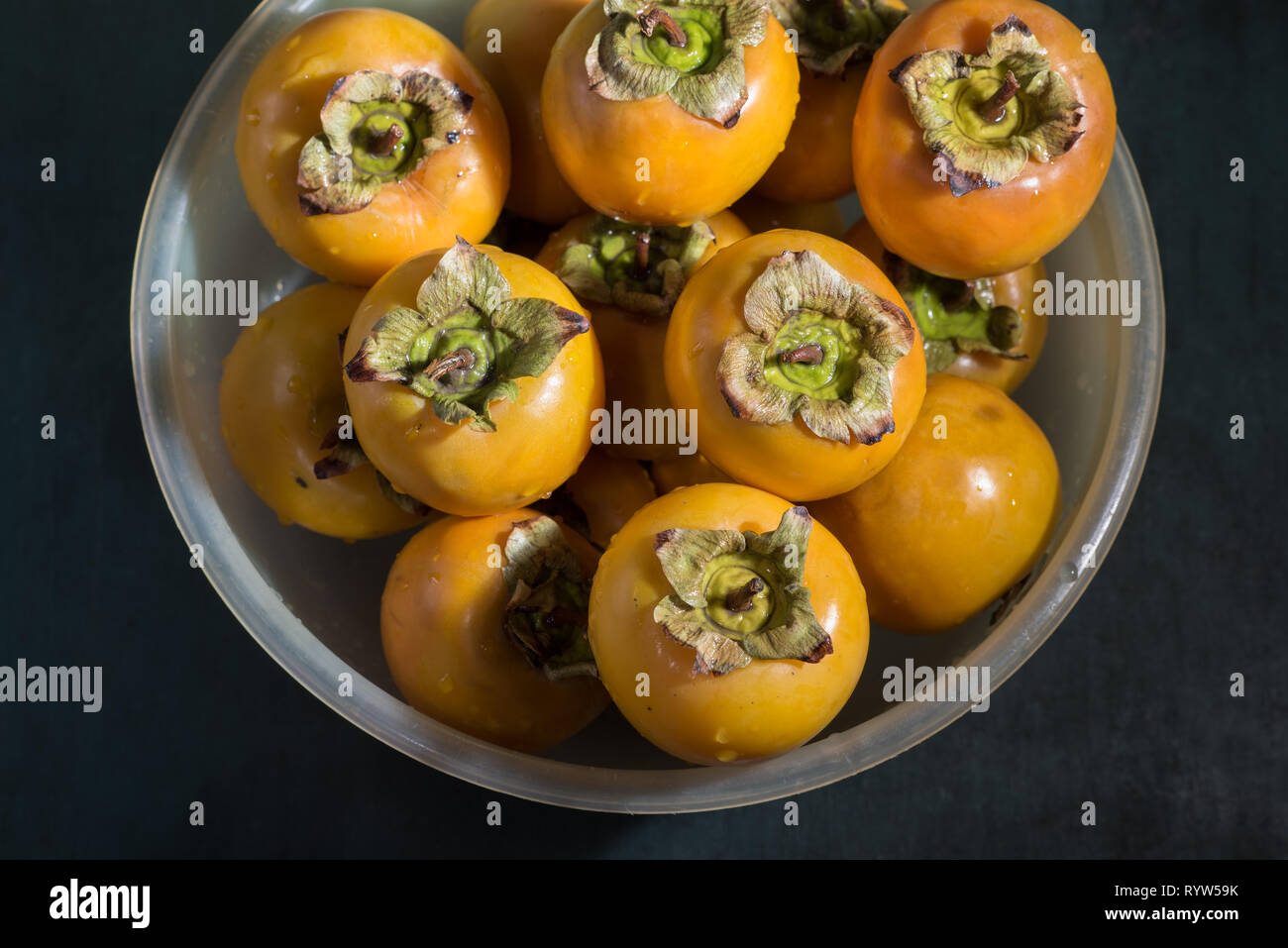 Washed wet persimmons in a bowl on the table, close up. Stock Photo