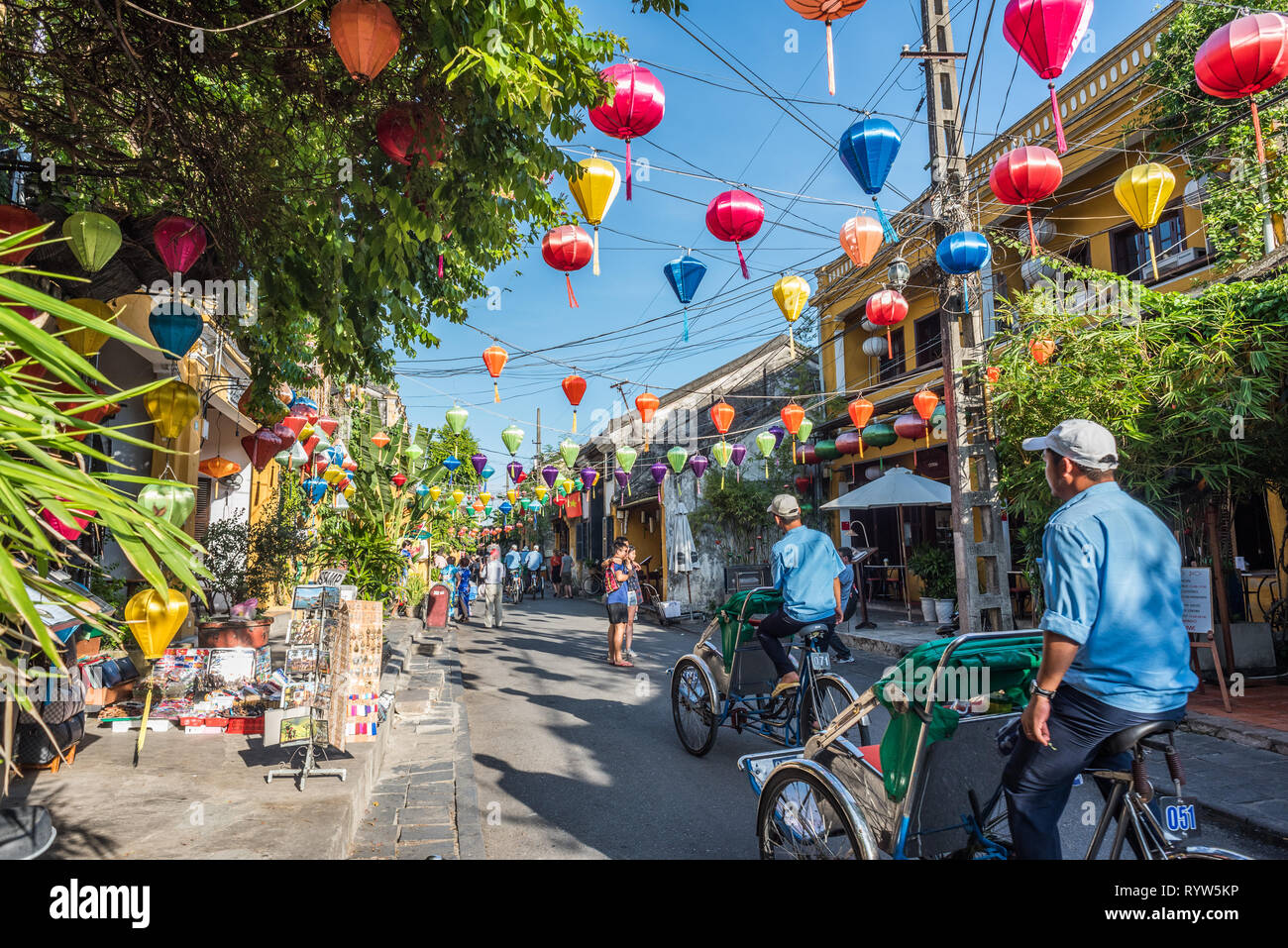 Hoi An, Vietnam - October 24, 2018: two rickshaws drive along a colorful street of the old town decorated by lanterns. Stock Photo