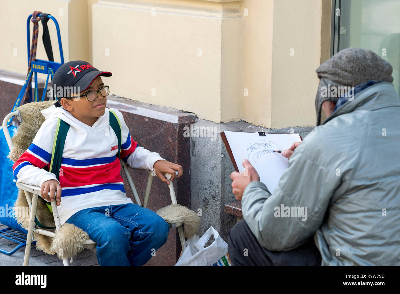 An elderly male artist paints a portrait of an Oriental-looking boy on Nevsky Prospect in St. Petersburg, Russia, September, 2018 Stock Photo