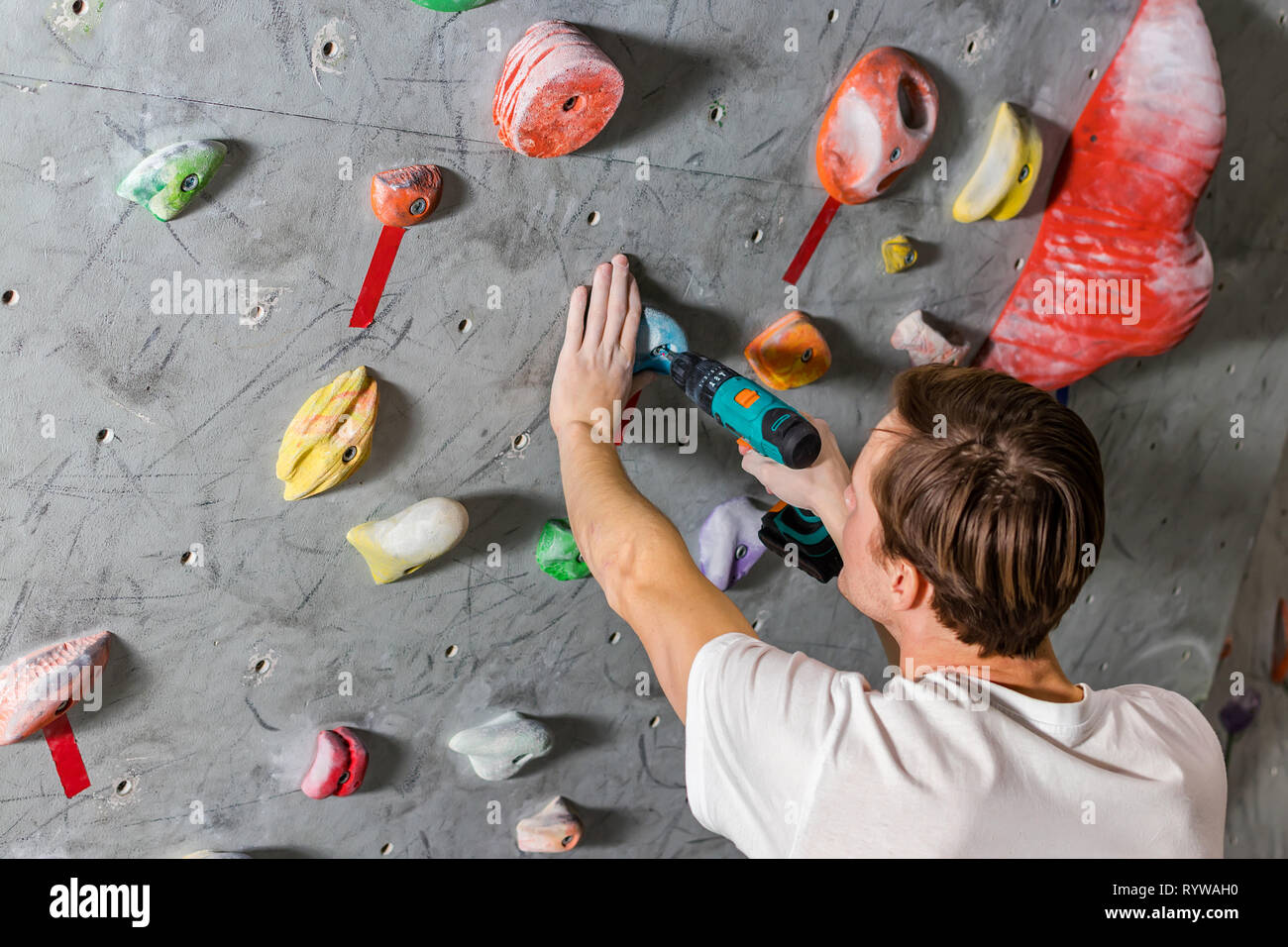 Rock climber fastens the hook with a screwdriver at the climbing wall