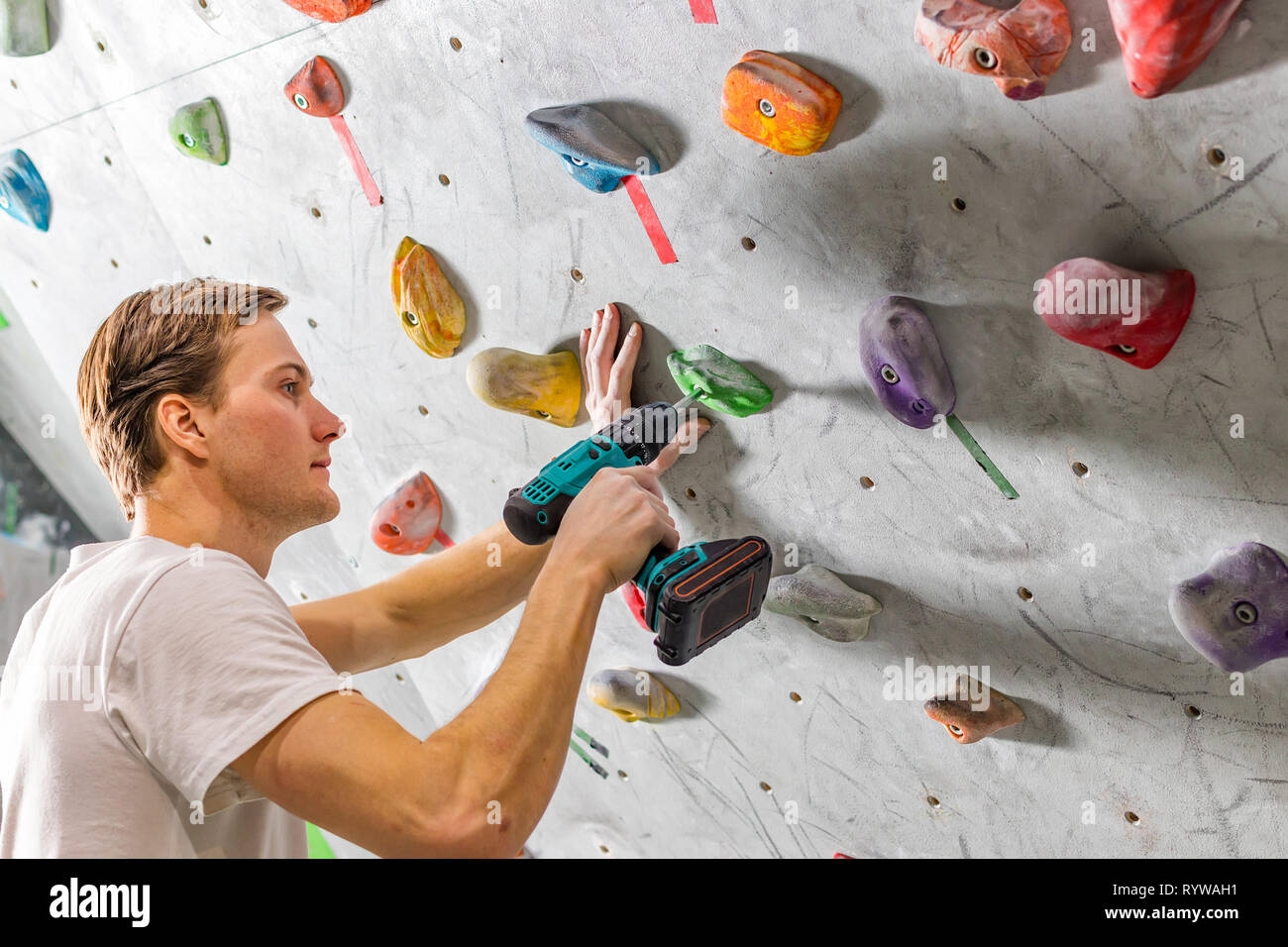 Rock climber fastens the hook with a screwdriver at the climbing wall
