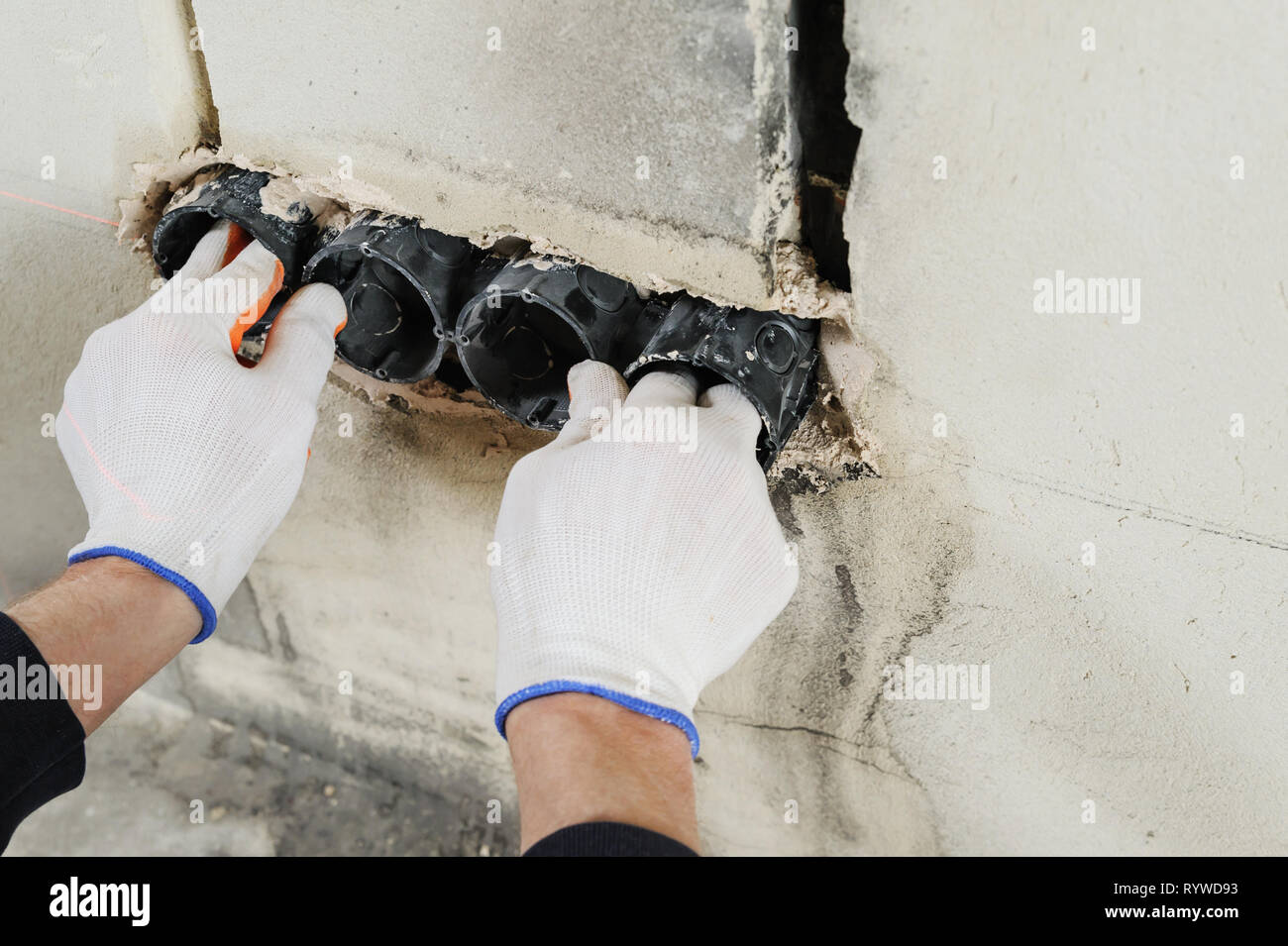 Installing electrical socket box. A worker attaches to the wall socket