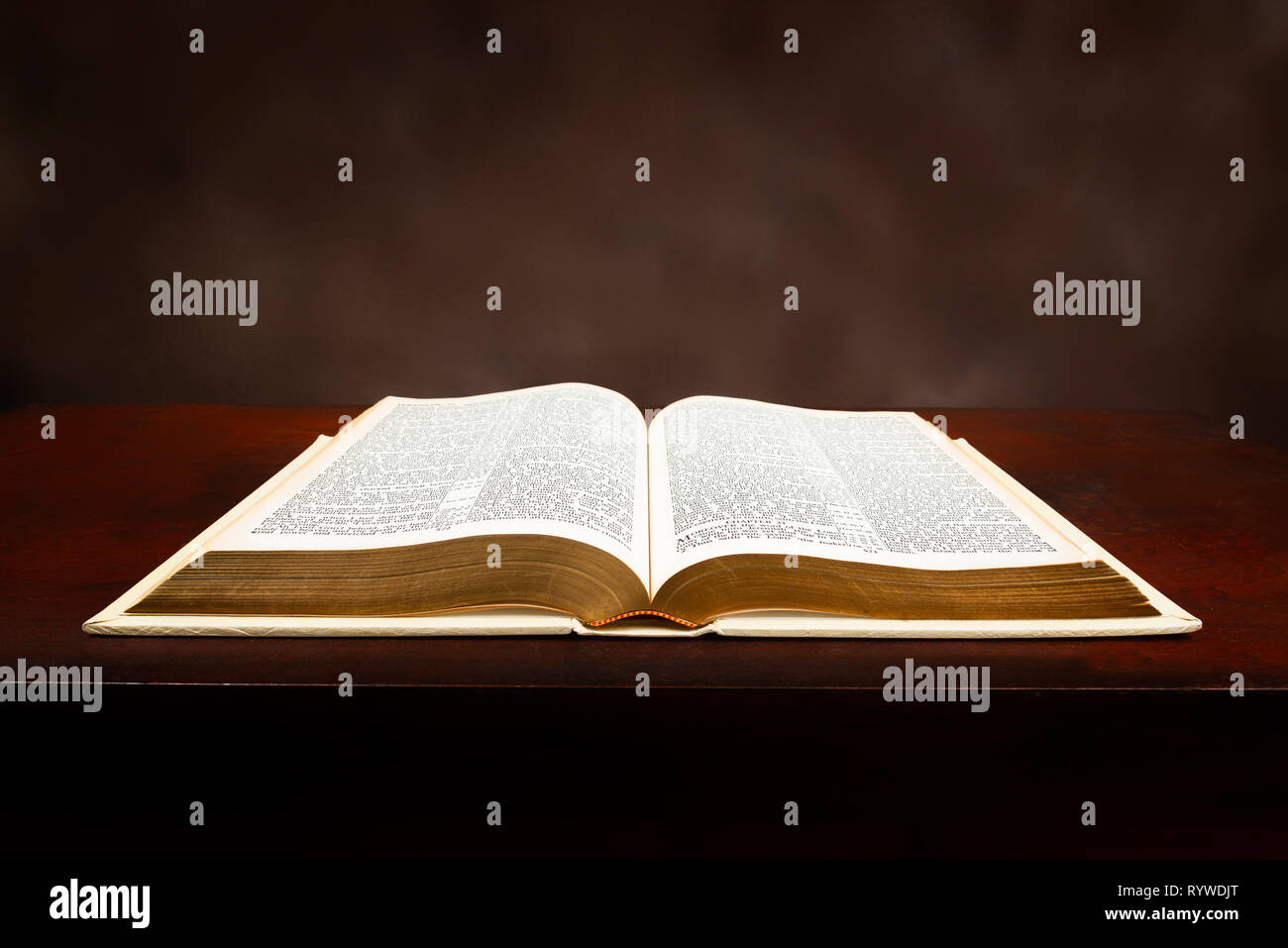 Horizontal close-up shot of an old Bible lying open on a brown background. Stock Photo