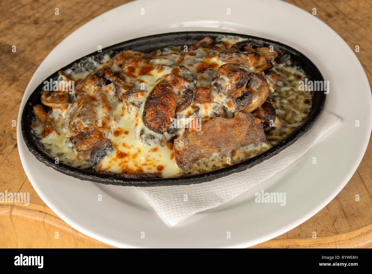 Sous vide (low temperature cooking) beef tongue with cheese and mushrooms.  Served in a ceramic vessel. On a wooden background Stock Photo - Alamy