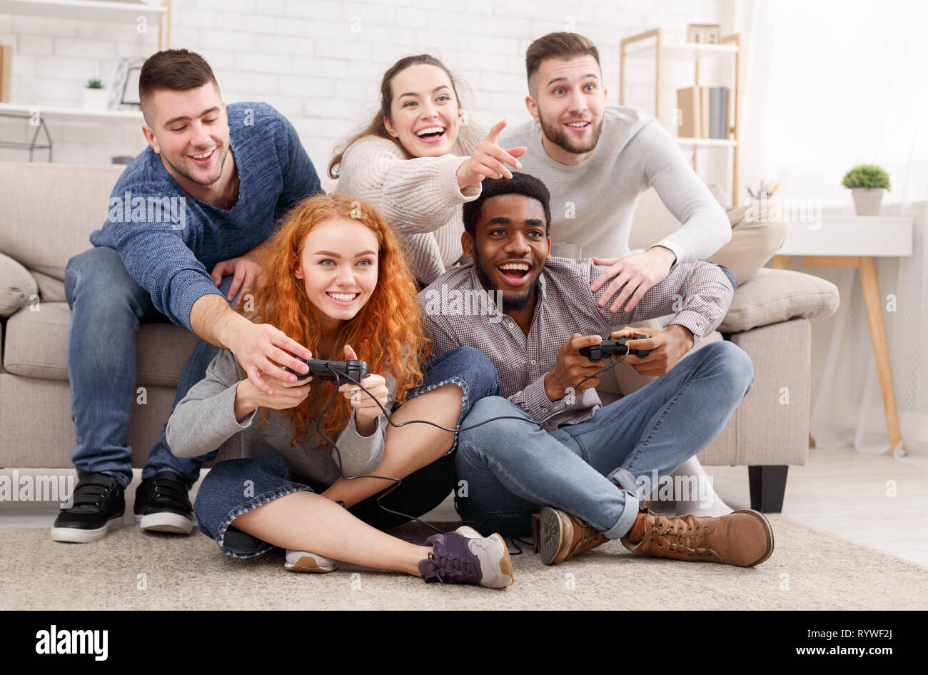Adult friends playing video games, sitting on floor at home Stock Photo