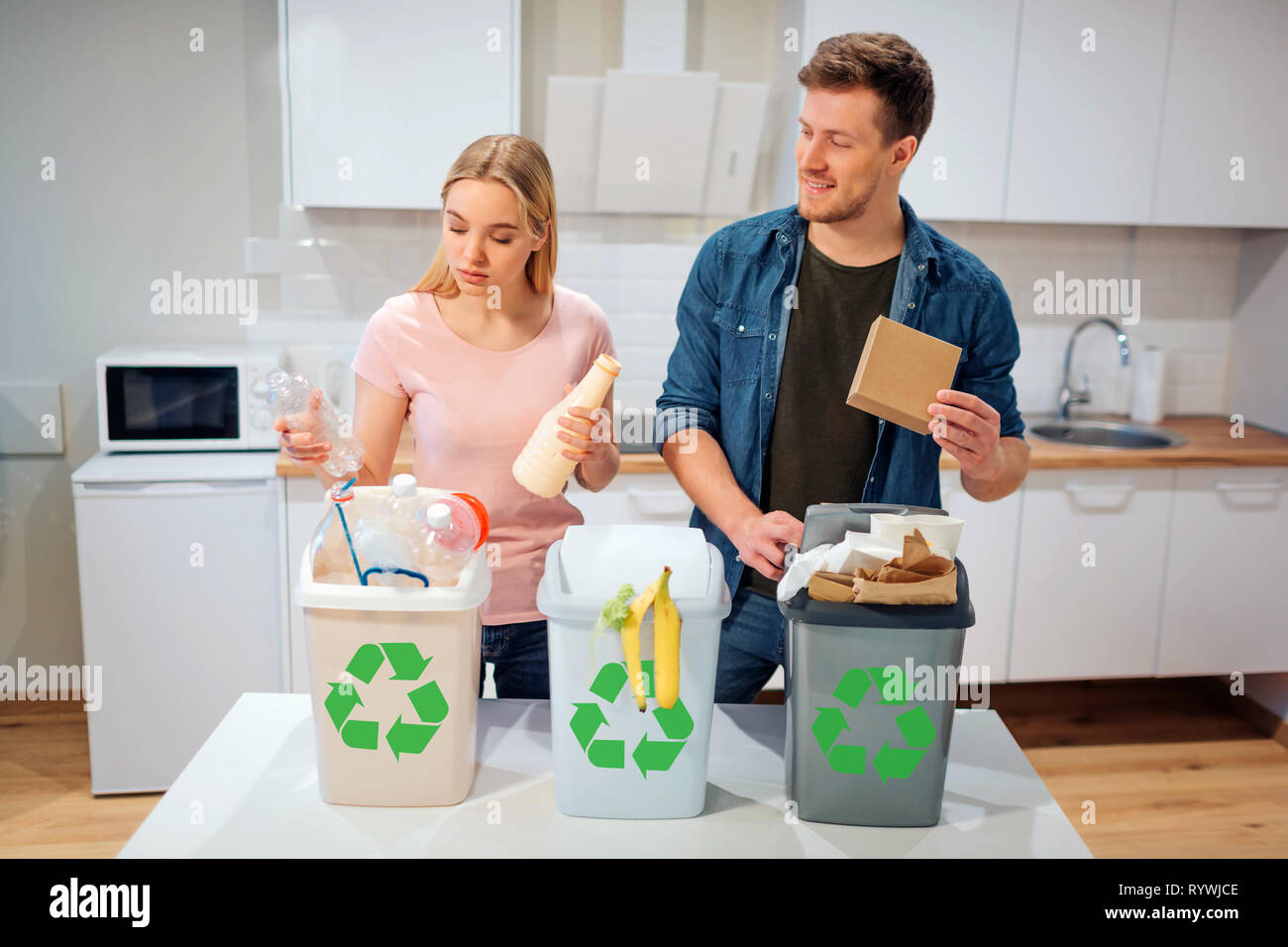 Waste sorting at home. Smiling young family putting plastic, paper, other waste in garbage bio bins in the kitchen Stock Photo